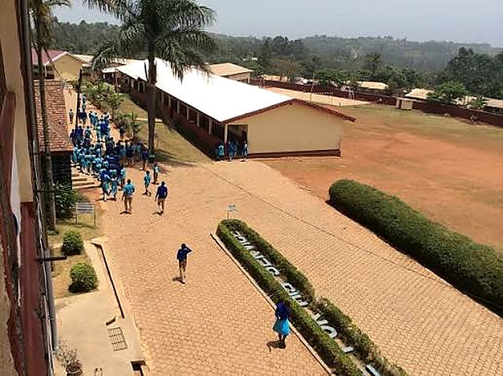 Aerial view of the PSS Bafut campus with students in sky-blue uniforms walking between the classroom blocks and the sports field